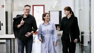 3 Personen gehen den Gang entlang und unterhalten sich fröhlich.