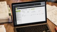 Notebook mit geöffneter Software von PROJEKT PRO steht auf dem Tisch. Ordner mit Rechnungen liegen leicht sichtbar daneben.