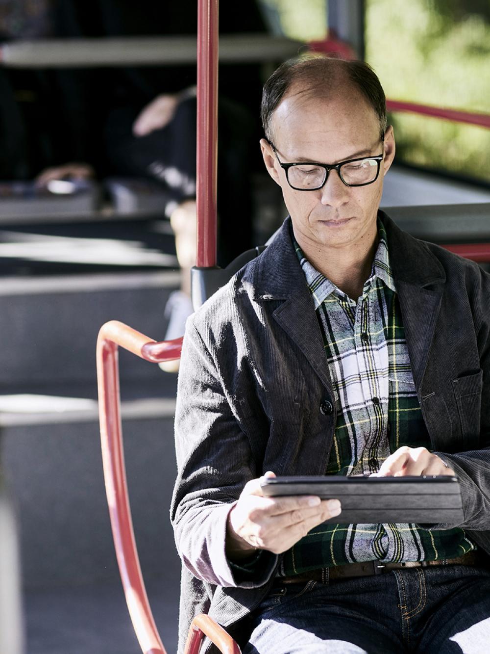 Mobile Arbeitszeiterfassung: Mann sitzt im Bus und erfasst Zeiten auf Tablet.