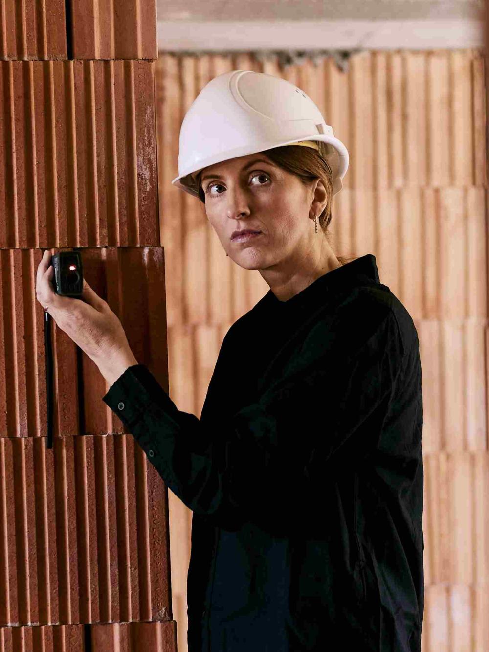 Frau auf Baustelle mit Helm misst etwas mit dem Laser aus.