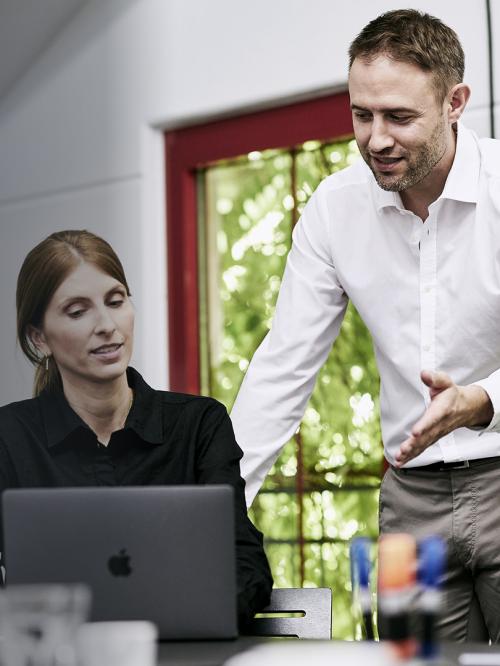 Trainer schult junge Architektin. Man sieht zwei Personen, die auf ein Notebook schauen.