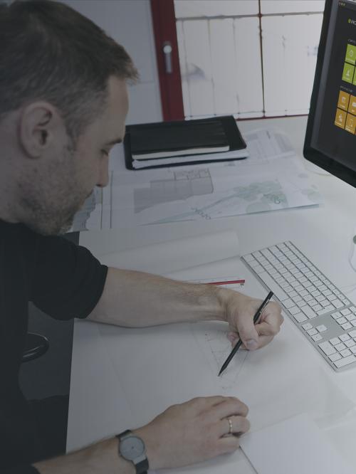 Zeichnende Person am Schreibtisch. Auf einem Bildschirm ist die Software PROJEKT PRO zu sehen.
