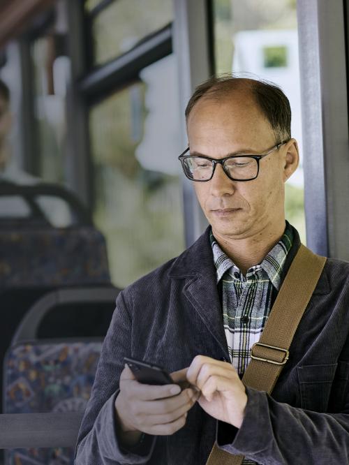Mann tippt auf Smartphone seine Arbeitszeit ein. Er steht in einem Bus.