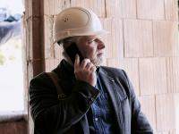Mann mit weißem Helm telefoniert auf der Baustelle.