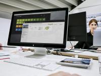 Bildschirm mit geöffneter Software von PROJEKT PRO. Im Hintergrund Architektin, die an einem anderen Schreibtisch arbeitet.