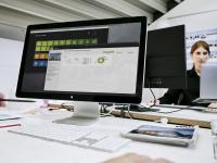 Bildschirm mit geöffneter Software von PROJEKT PRO. Im Hintergrund Architektin, die an einem anderen Schreibtisch arbeitet.